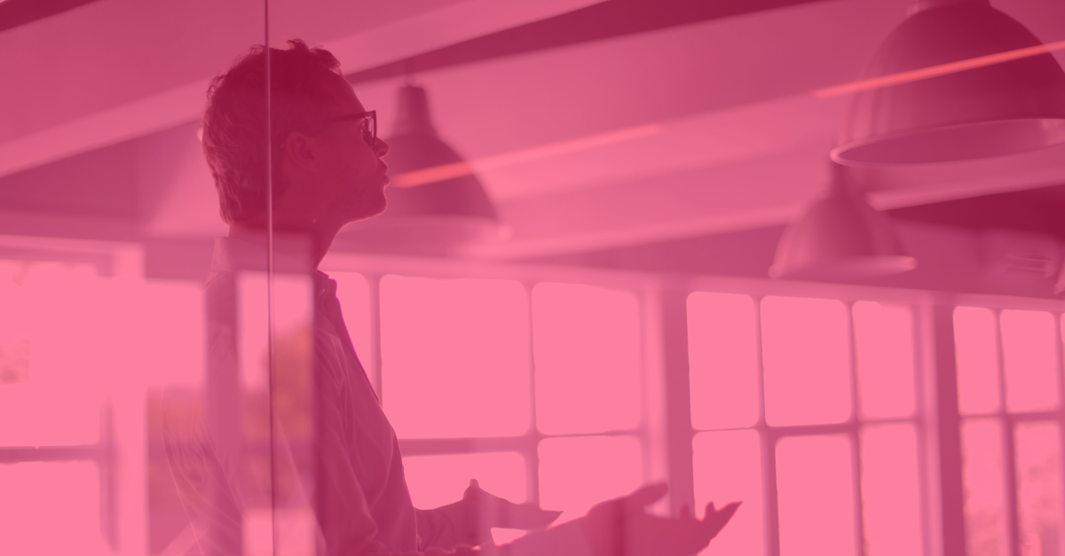 man in glass office speaking with his hands up as if explaining something with a red filter over the image